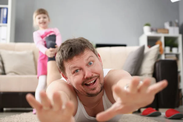 Kız babasının ayağını çekiyor ve oynamak istiyor, adam evde yerde çığlık atıyor. — Stok fotoğraf