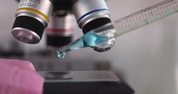 Científico gotea líquido azul en primer plano de vidrio microscopio — Vídeos de Stock