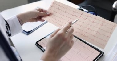 Klinikte kağıt üzerinde elektrokardiyogram ve dijital tablet üzerinde çalışan bir doktor.