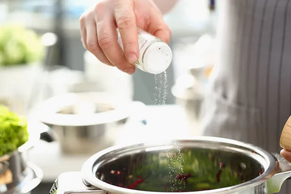 Cocinero profesional mantenga la bodega de sal y añadir sal a la sopa contra el fondo de la cocina — Foto de Stock