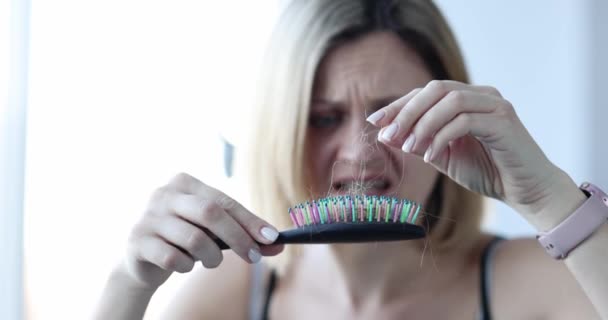 Woman looks in horror at comb with fallen hair closeup — Stock Video