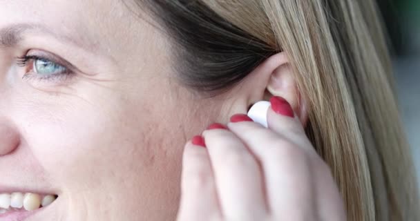 Улыбающаяся красивая женщина вставляет беспроводные наушники в ухо крупным планом — стоковое видео
