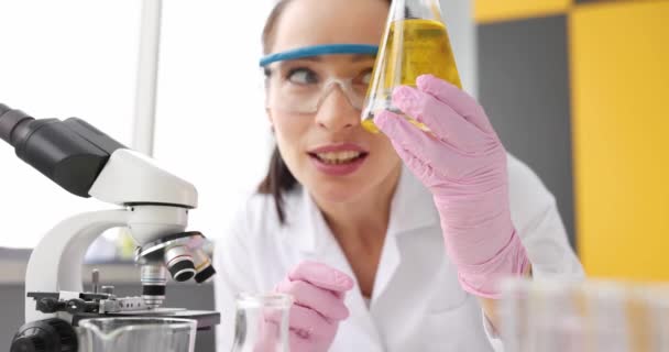 Kobieta-naukowiec dokładnie bada kolbę z przezroczystym żółtym laboratorium olejowym — Wideo stockowe