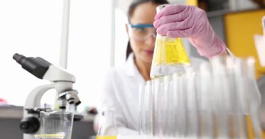 Bilimadamları koruyucu eldivenleriyle şişenin içinde sarı bir sıvı tutuyor.