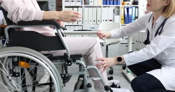 Врач стучит молотком по нервным окончаниям ноги пациента в инвалидном кресле — стоковое видео