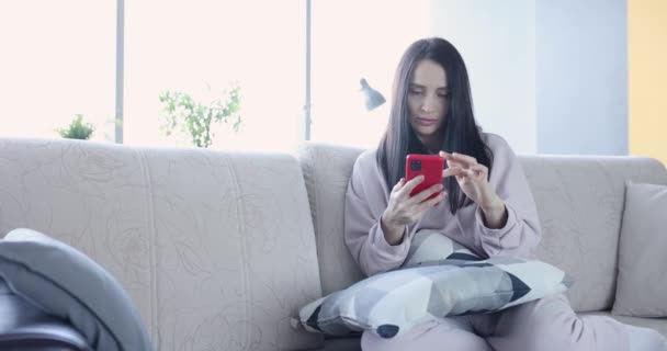 Mujer triste se sienta en el sofá y mira en el teléfono inteligente — Vídeos de Stock