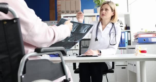 Doctor toont x-ray van wervelkolom naar patiënt in rolstoel — Stockvideo