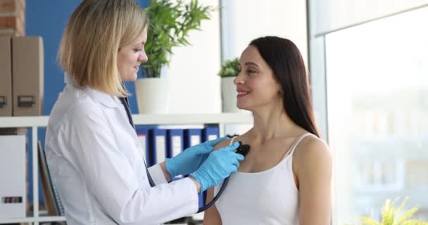 Doctor with stethoscope listens to lungs of female patient in clinic — Stock Video