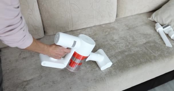 Женщина пылесосит диван с беспроводным пылесосом — стоковое видео
