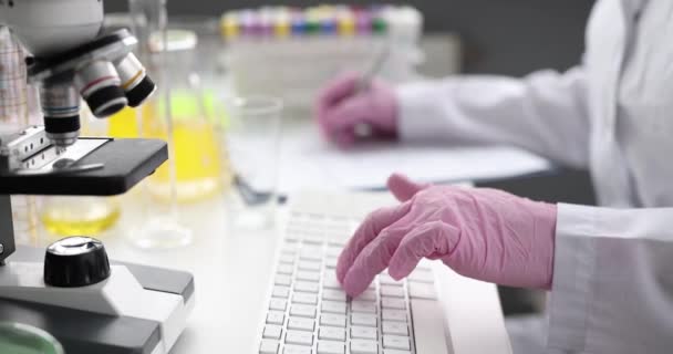 Naukowiec w rękawiczkach pisze na klawiaturze w laboratorium. — Wideo stockowe