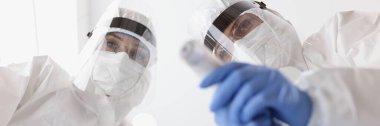 Koruyucu giysili doktor hasta maskesi takıyor ve alttaki sıcaklığı ölçüyor.