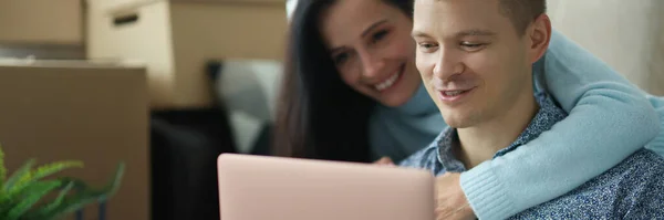 Νεαρό παντρεμένο ζευγάρι επικοινωνεί σε κοινωνικά δίκτυα χρησιμοποιώντας φορητό υπολογιστή στο διαμέρισμα με κουτιά — Φωτογραφία Αρχείου