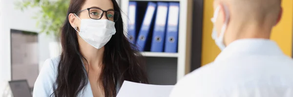 Zakenvrouw in beschermend medisch masker met documenten en een gesprek met een man in functie — Stockfoto