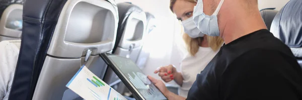 Hombre y mujer en máscaras médicas protectoras volando en avión y discutiendo diagrama en documentos — Foto de Stock