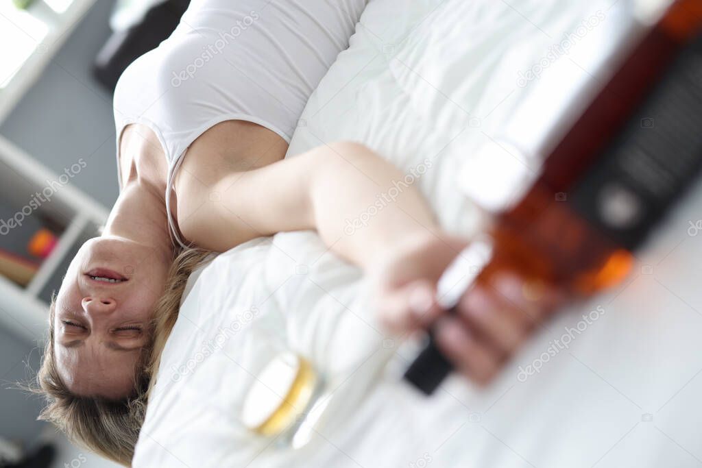 Drunk woman sleeping with bottle of alcohol in bed closeup