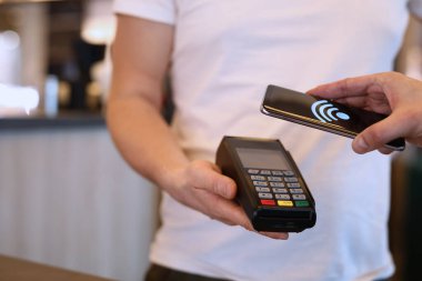 Man paying with mobile phone over pos terminal with nfc technology