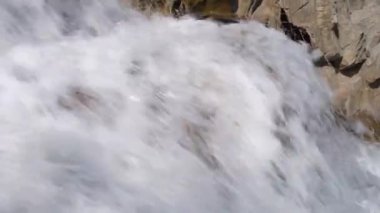 Waves of a mountain river splash in strong stream against the stones and boulders of cascade