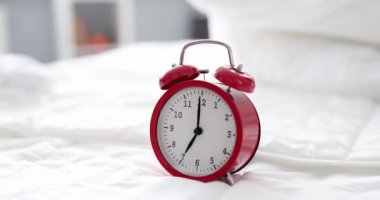 Red alarm clock for seven in morning is on bed