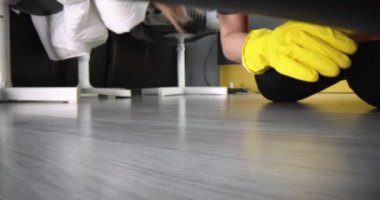 Cleaning woman in gloves takes out socks from under bed