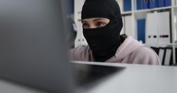 Swindler in balaclava looks through magnifying glass at computer monitor — ストック動画