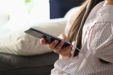 Kanepede oturan akıllı telefonlu ve müzik dinleyen bir kadın.