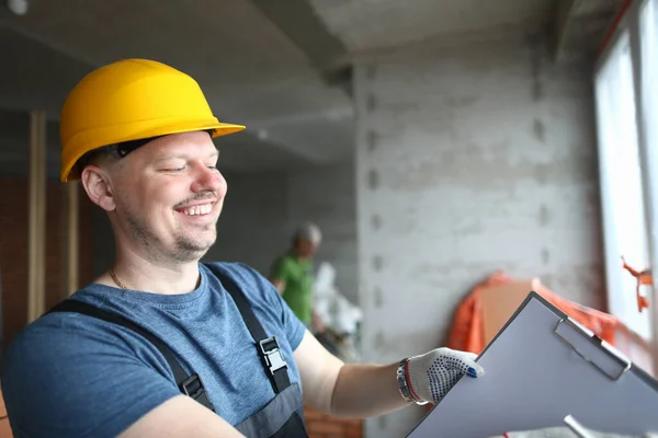 Constructor sonriente sujetando el portapapeles y anotando el material de trabajo necesario para la renovación — Foto de Stock