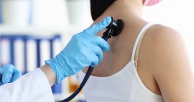 Steteskoplu doktor klinikte muayene sırasında kadınların nefes alışlarını dinler.