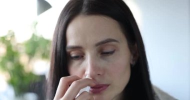 Woman with severe runny nose holds medicine spray into nose in hand