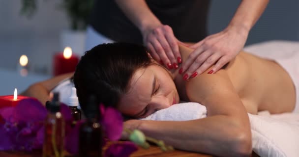 Woman enjoys spa resort while lying on table treatment procedure next to candle — Vídeos de Stock