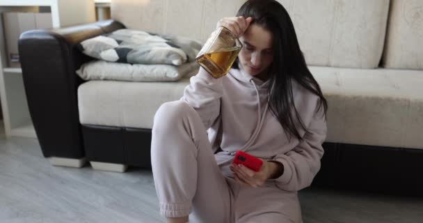 Lonely depressed woman holding smartphone and bottle of alcohol — ストック動画