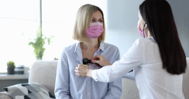 Koruyucu maskeli doktor, evde zatürree olduğundan şüphelenilen bir kadının ciğerlerini dinliyor. — Stok video