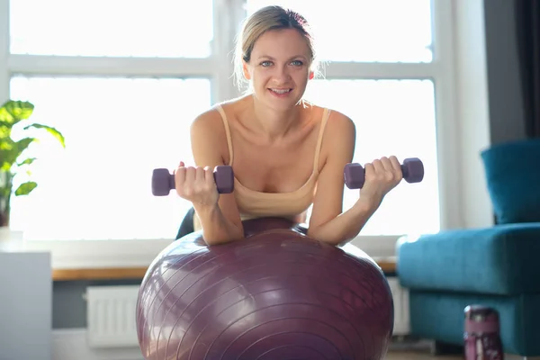 Mulher sorrindo fazendo exercício com halteres na bola de fitness — Fotografia de Stock