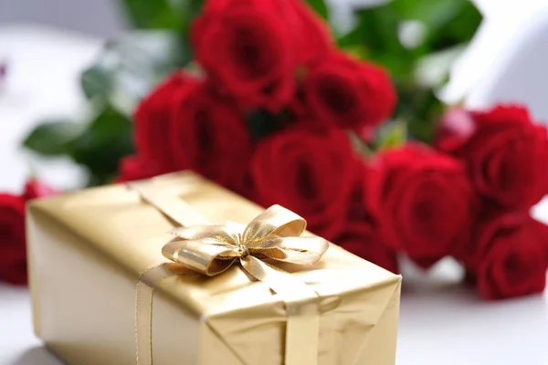 Arany ajándékdoboz és vörös rózsa csokor — Stock Fotó