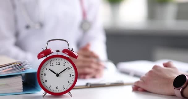 Doctor communicates with patient of clinic on table is alarm clock — Stockvideo