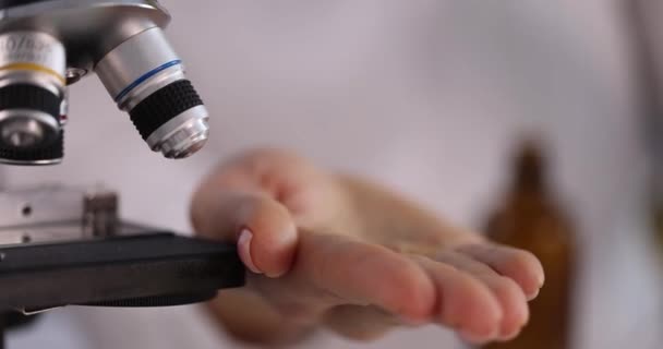 Scientist drips transparent liquid on palm near microscope — Stock video