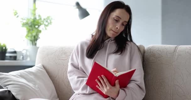 Glimlachende vrouw die dagboekaantekeningen schrijft terwijl ze thuis op de bank zit — Stockvideo