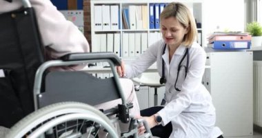 Doktor tekerlekli sandalyedeki hastanın dizine çekiç darbesi uyguluyor.