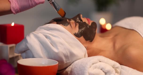 Woman receiving skin treatment in beauty salon. Cosmetologist applies mask to skin of face — Stock Video
