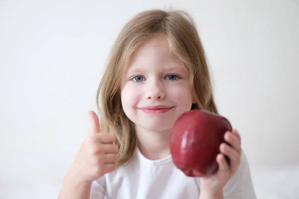 Smiling girl holding thumbs up and holding ripe apple — Fotografia de Stock