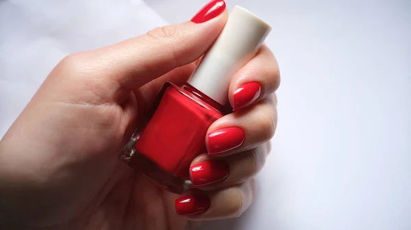 Ongles femelles tient bouteille de vernis à ongles rouge vif — Photo