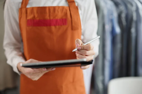 Dry cleaning company worker in uniform, girl hold tablet device with pen, high quality service