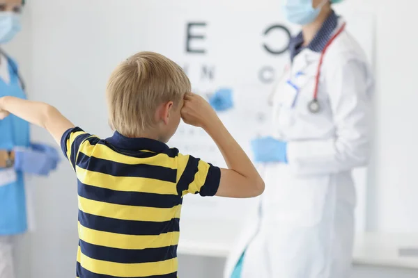 Boy on appointment in clinic, oculist cabinet, sight diagnostic closing eye and say out loud letter on board — Zdjęcie stockowe