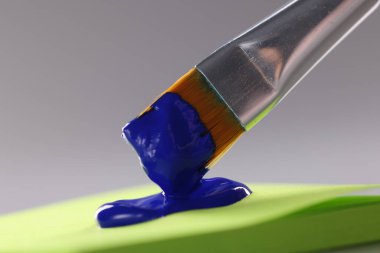 Mavi boyayla kaplı fırça, yeşil kağıda damlayan mavi renk.