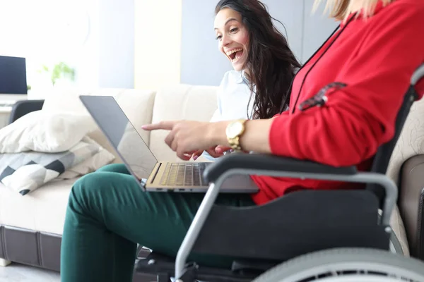 Друзі проводять час вдома, дивлячись фільм і сміючись, жінка в інвалідному візку з ноутбуком на колінах — стокове фото