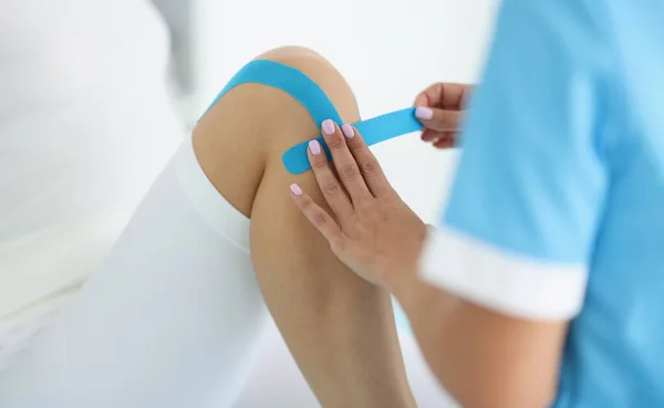 Fyzioterapeut vložil kineziologickou pásku na koleno klienta, odstranil bolest, rehabilitační centrum — Stock fotografie