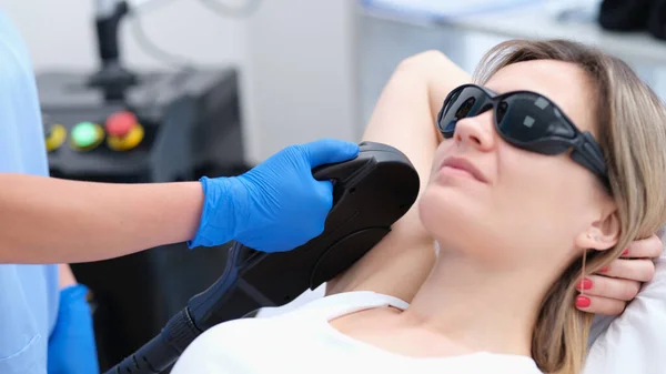 Woman client in protective glasses having laser hair removal of armpit in beauty salon — стоковое фото