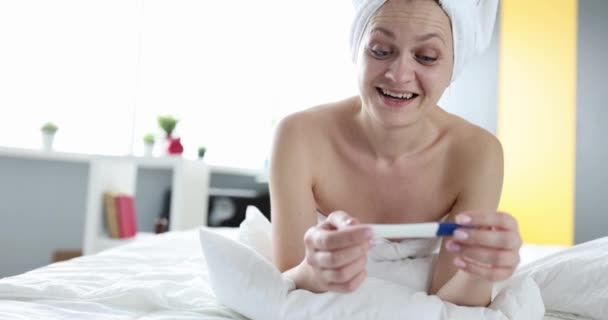 Smiling happy woman holding positive pregnancy test lying on bed — Video
