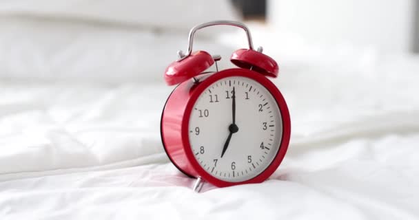 Red alarm clock for seven in morning stands on white bed — Stok video
