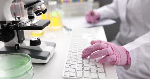 Researcher works at table and types on keyboard with microscope — Stock videók