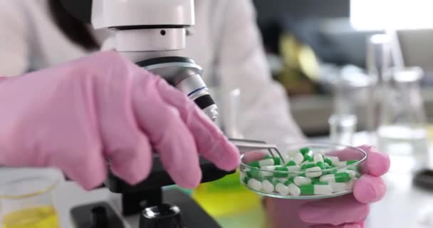 Химик-женщина изучает медицинские таблетки или лекарства под микроскопом — стоковое видео